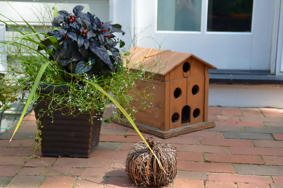 Decorative planter and wood garden accent on brick patio near house door.